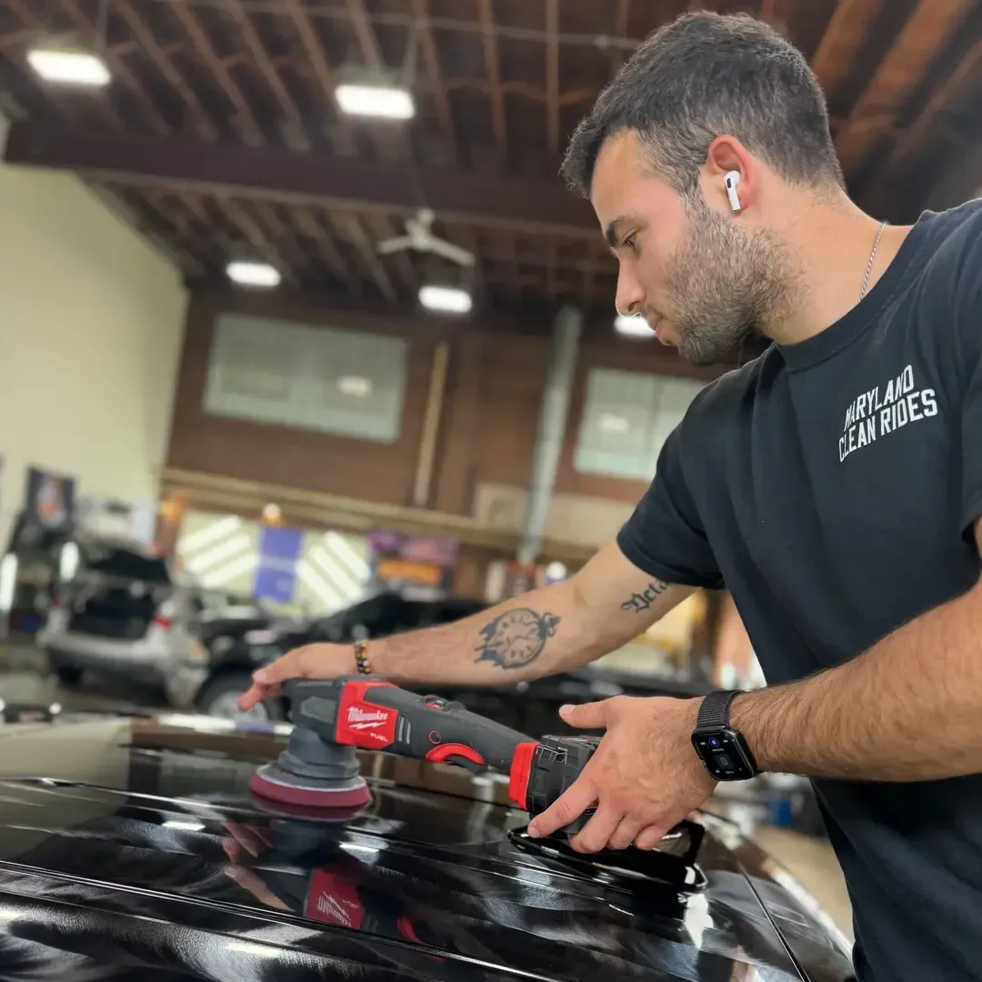 Man using a power polisher on a black car in a workshop.